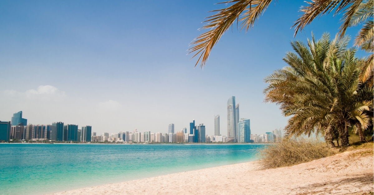 Luxury beach view of Abu Dhabi with turquoise water and city skyline, representing international travel opportunities for private governesses.