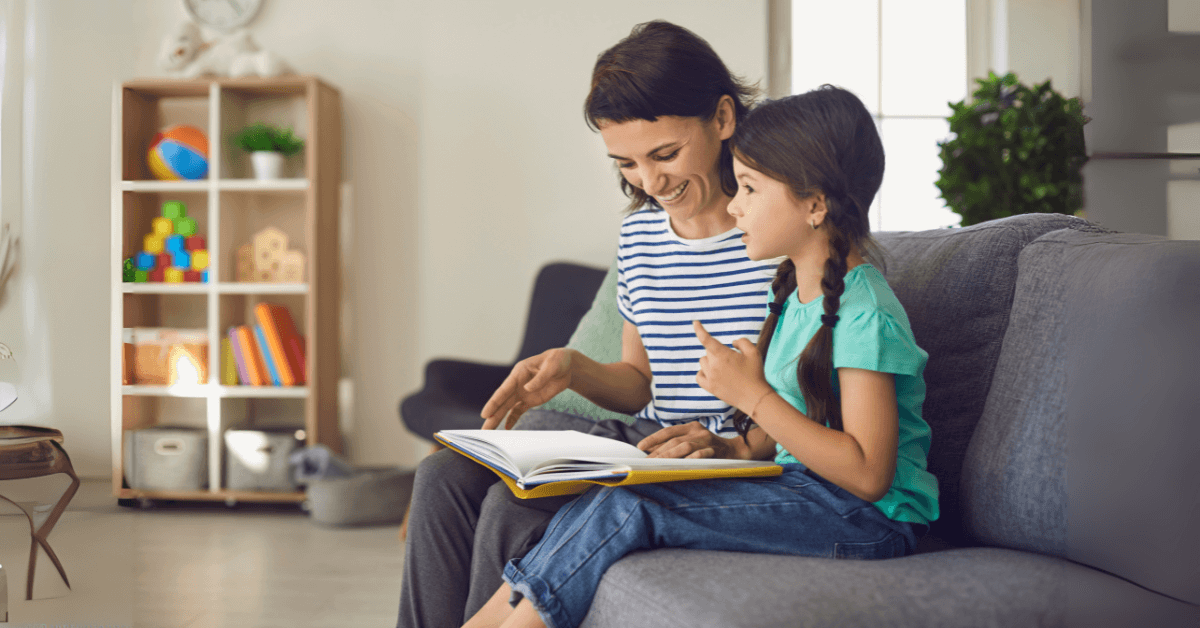 A nanny reads a book with a young girl during a nanny trial, both smiling and engaged. The cozy living room setting features educational toys and books, illustrating a warm, professional approach to how to ace a nanny trial.